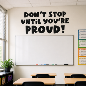 Don't Stop Until You're Proud wall decal in a classroom above a whiteboard, bold playful black lettering